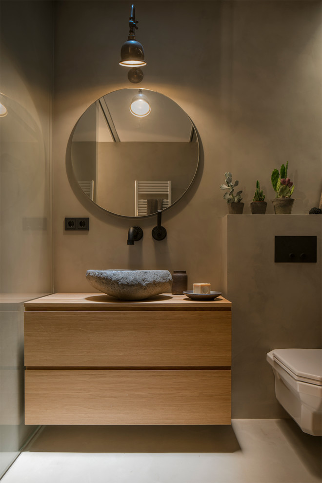 Bild på ett mellanstort brun brunt badrum med dusch, med möbel-liknande, skåp i mellenmörkt trä, en toalettstol med hel cisternkåpa, grå väggar, betonggolv, ett fristående handfat, träbänkskiva och grått golv