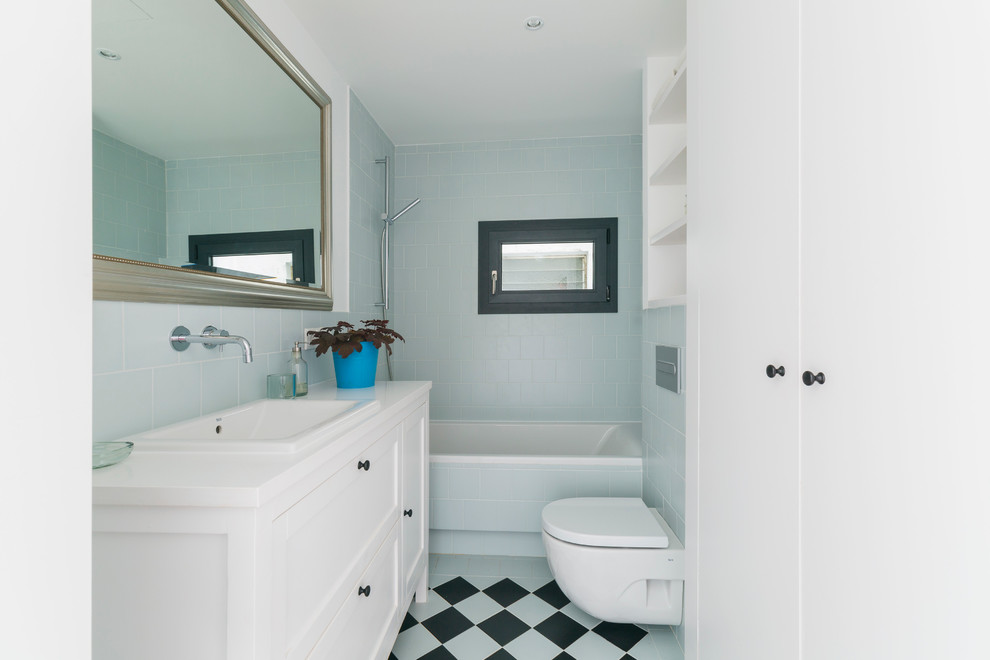 Exemple d'une salle de bain principale chic de taille moyenne avec un lavabo posé, des portes de placard blanches, une baignoire en alcôve, un combiné douche/baignoire, WC suspendus, un carrelage bleu, un mur blanc, des carreaux de céramique, un sol en carrelage de céramique, un plan de toilette en surface solide, une fenêtre et un placard à porte shaker.