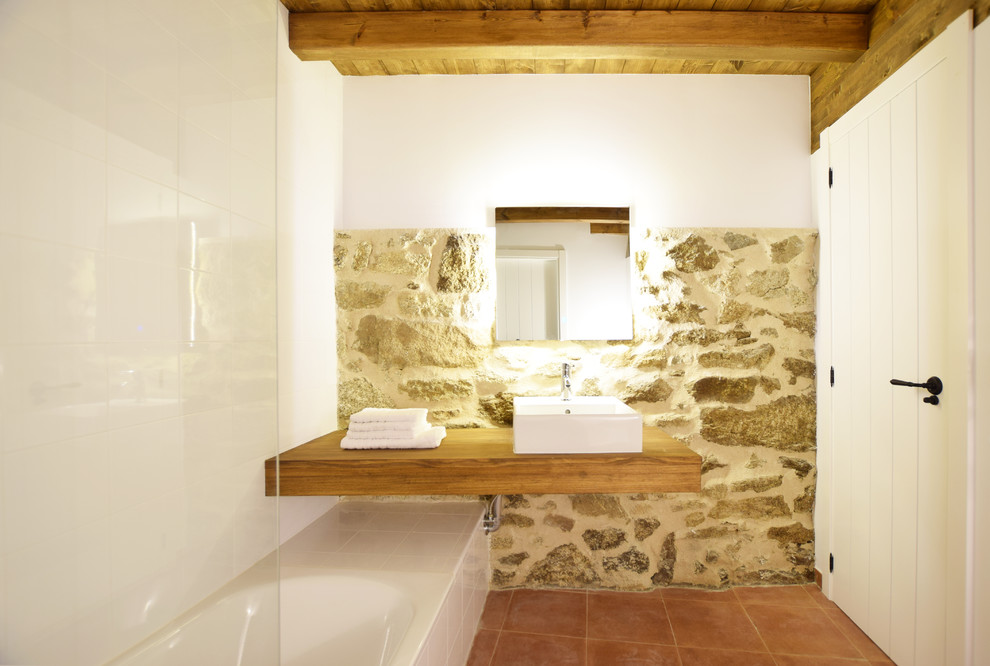 Ejemplo de cuarto de baño mediterráneo con bañera empotrada, combinación de ducha y bañera, paredes blancas, lavabo sobreencimera, encimera de madera y suelo rojo