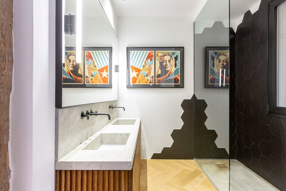 Modern inredning av ett grå grått badrum, med skåp i mellenmörkt trä, en kantlös dusch, svart kakel, vita väggar, ljust trägolv, ett integrerad handfat, beiget golv, med dusch som är öppen och släta luckor
