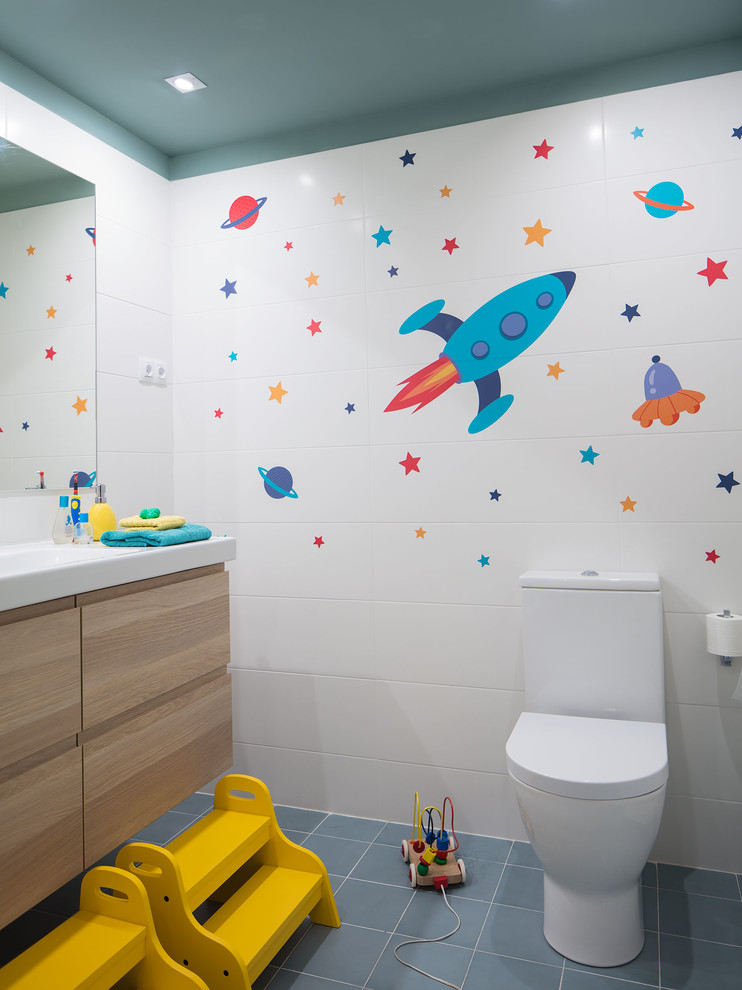 Ispirazione per una piccola stanza da bagno per bambini design con ante lisce, ante in legno chiaro, WC a due pezzi, piastrelle bianche, piastrelle in ceramica, pareti bianche, pavimento con piastrelle in ceramica, lavabo integrato, top in superficie solida e pavimento blu