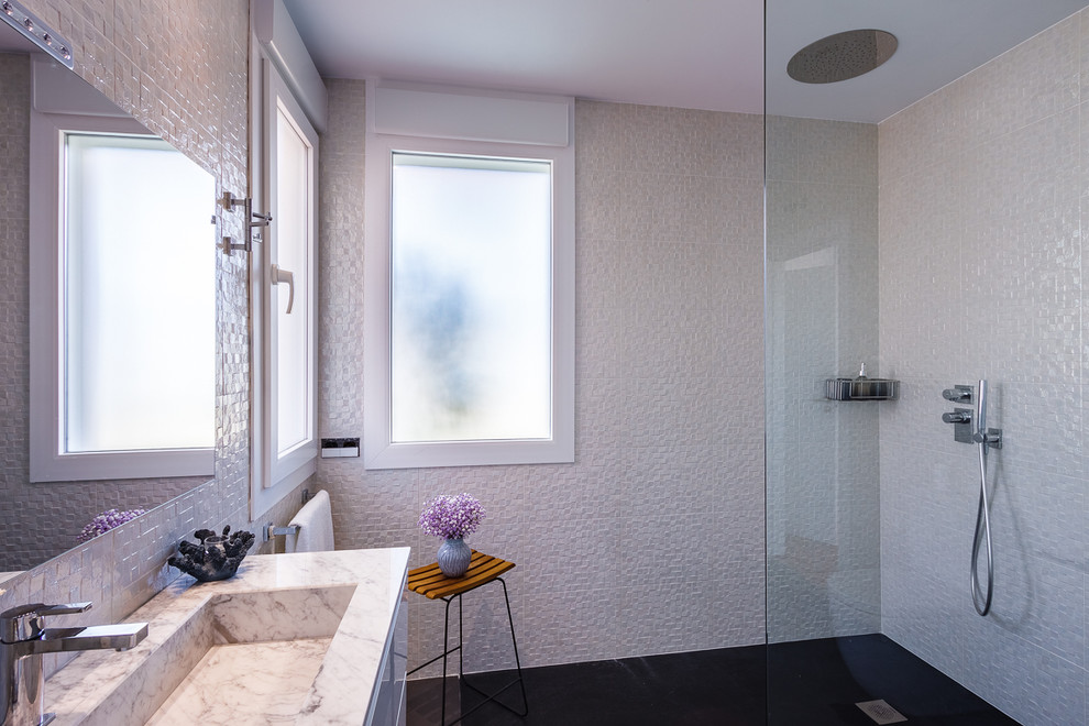 Exempel på ett mellanstort modernt en-suite badrum, med släta luckor, vita skåp, en kantlös dusch, en toalettstol med hel cisternkåpa, vit kakel, keramikplattor, vita väggar, skiffergolv, ett avlångt handfat, marmorbänkskiva, svart golv och med dusch som är öppen