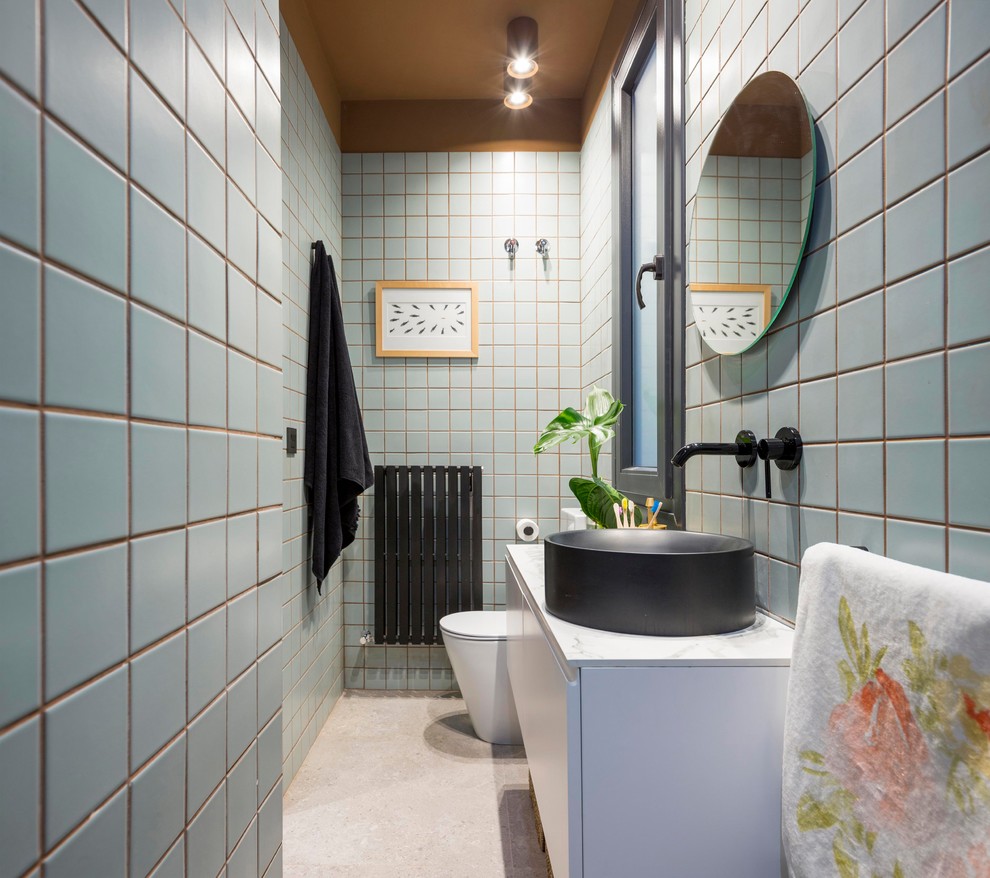 Cette image montre une petite salle de bain design avec un placard à porte plane, des portes de placard blanches, un carrelage bleu, des carreaux de céramique, une vasque et un plan de toilette en marbre.