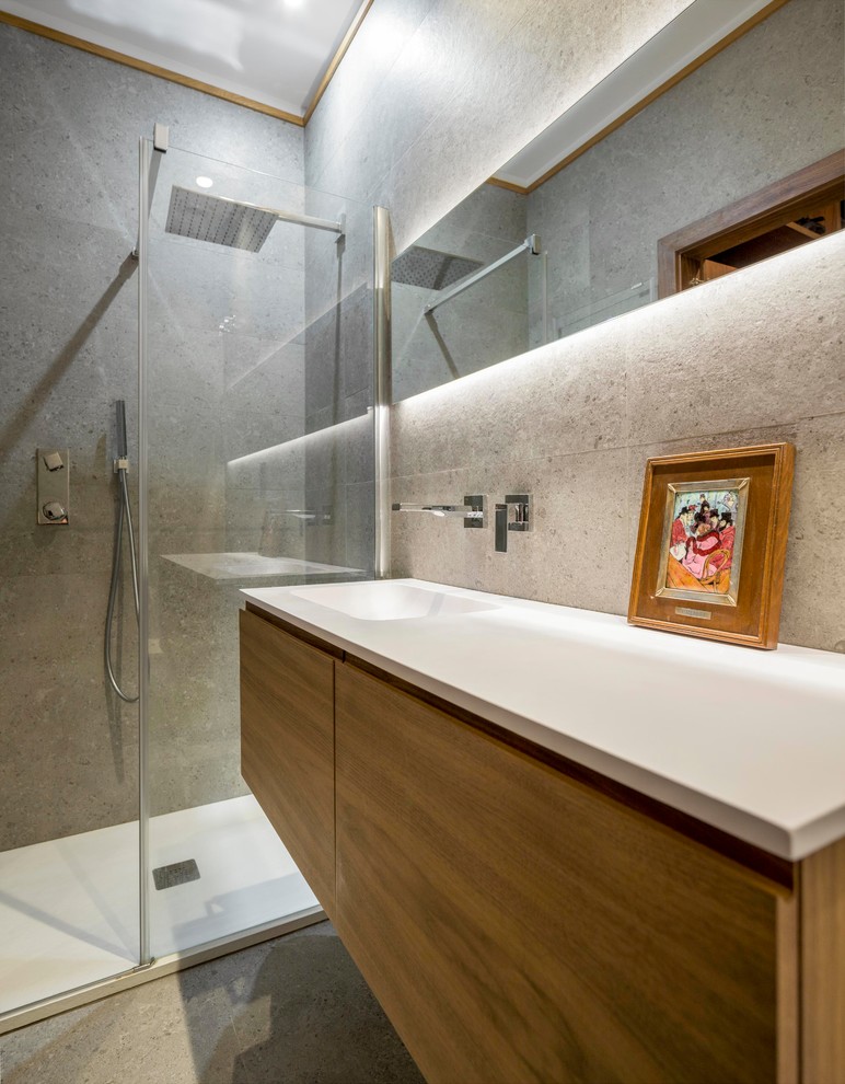 Réalisation d'une salle de bain design en bois brun de taille moyenne avec un placard à porte plane, un lavabo intégré, un carrelage gris, un mur gris, un sol gris et un plan de toilette blanc.