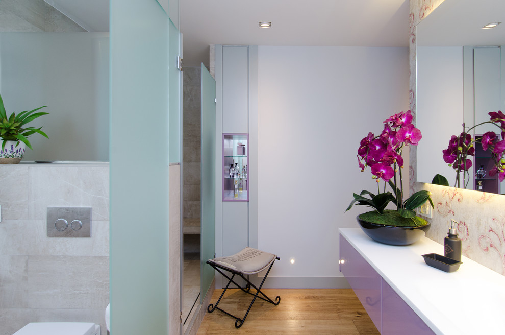 Cette photo montre une grande salle de bain tendance avec un placard en trompe-l'oeil, des portes de placard violettes, WC à poser, un mur rose, un sol en bois brun et une vasque.