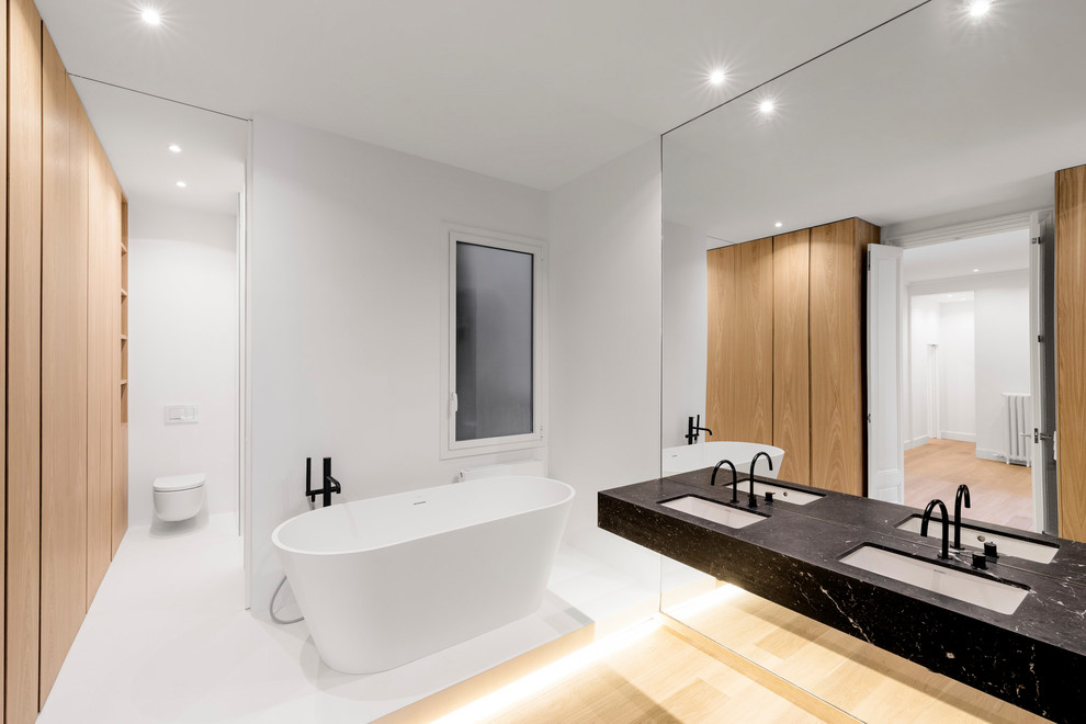 Modelo de cuarto de baño principal minimalista con bañera exenta, encimeras negras, paredes blancas y lavabo bajoencimera