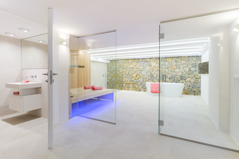 Diseño de sauna actual con puertas de armario blancas, bañera exenta, paredes blancas, lavabo integrado, suelo beige, encimeras blancas y piedra
