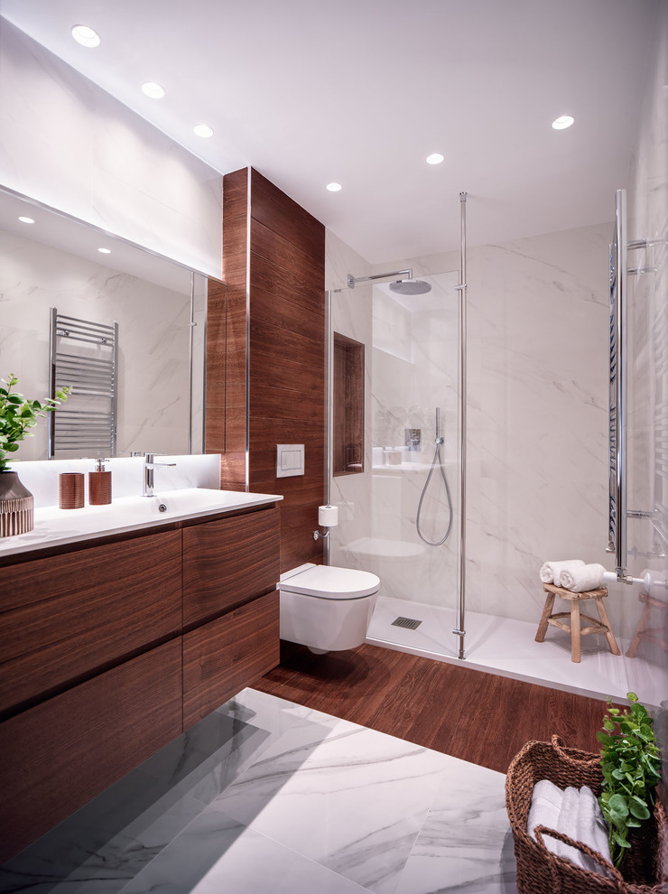 Exemple d'une salle de bain tendance en bois brun avec un placard à porte plane, WC suspendus, un mur blanc, un lavabo intégré, un sol multicolore et un plan de toilette blanc.