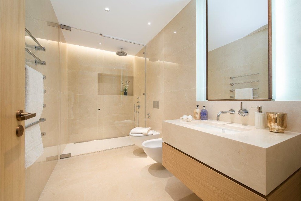 Cette image montre une grande salle de bain design en bois clair avec un placard à porte plane, un mur beige, un sol en marbre, un plan de toilette en marbre et un lavabo encastré.