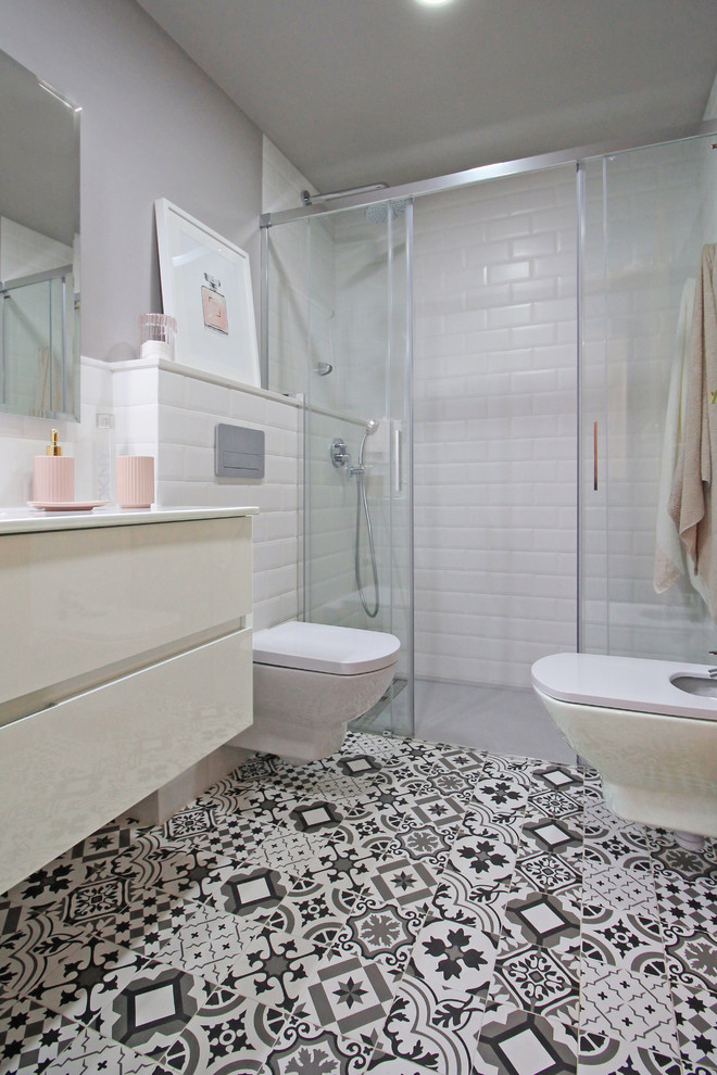 Exempel på ett mellanstort modernt vit vitt badrum med dusch, med en kantlös dusch, en vägghängd toalettstol, vit kakel, tunnelbanekakel, grå väggar, mosaikgolv, ett integrerad handfat, dusch med skjutdörr, släta luckor och vita skåp