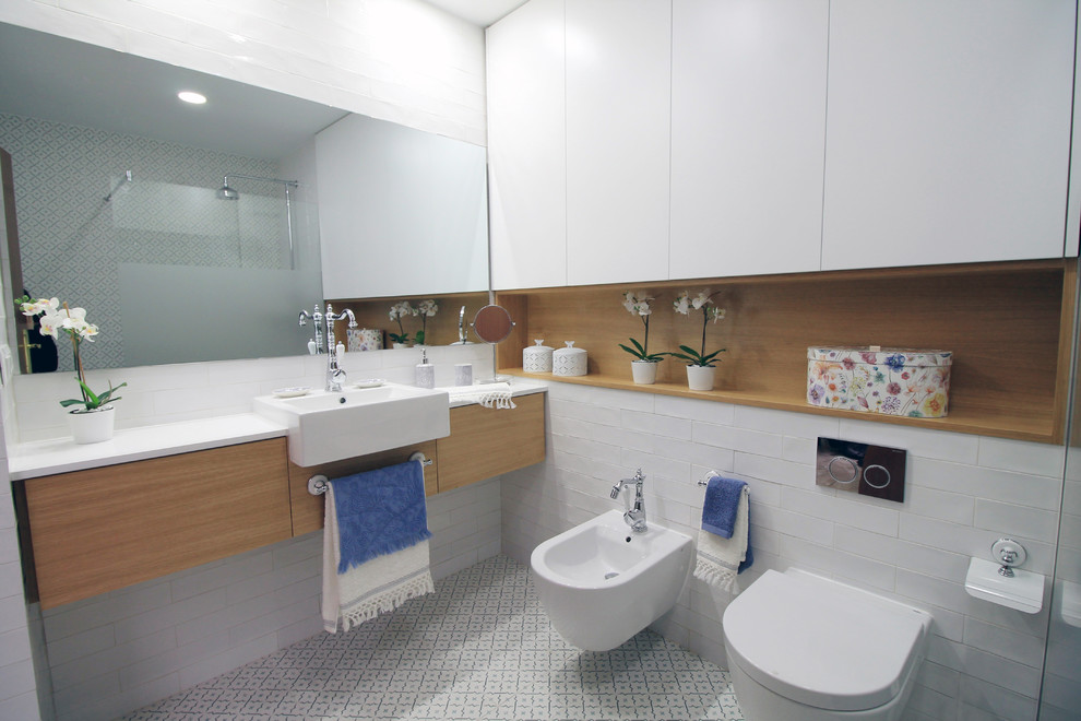 Idéer för att renovera ett mellanstort funkis vit vitt en-suite badrum, med släta luckor, en kantlös dusch, en vägghängd toalettstol, vit kakel, tunnelbanekakel, vita väggar, klinkergolv i keramik, ett fristående handfat, skåp i mellenmörkt trä och vitt golv