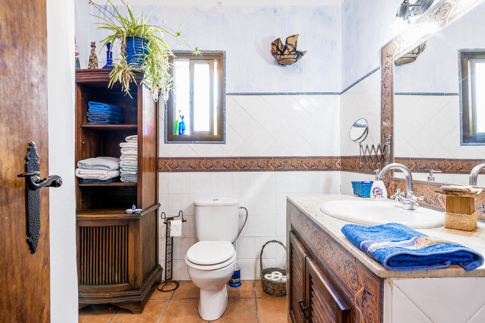 Idee per una stanza da bagno mediterranea con ante a persiana, ante marroni, WC a due pezzi, piastrelle in ceramica, pareti multicolore, lavabo da incasso, pavimento marrone e top beige