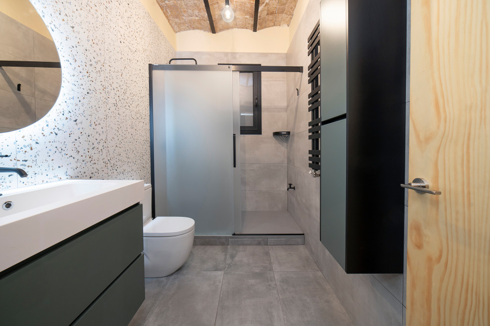 Large industrial ensuite bathroom in Barcelona with flat-panel cabinets, black cabinets, a built-in shower, a one-piece toilet, grey tiles, ceramic tiles, ceramic flooring, a trough sink, grey floors, a sliding door, white worktops, an enclosed toilet, a single sink, a floating vanity unit and a vaulted ceiling.