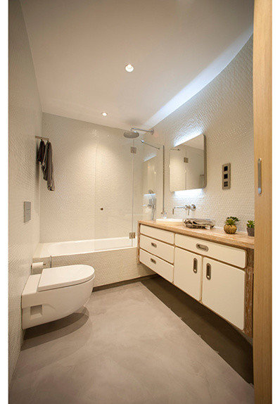 Immagine di una stanza da bagno padronale design di medie dimensioni con vasca ad alcova, vasca/doccia, WC sospeso, pareti bianche, pavimento in cemento e lavabo a bacinella