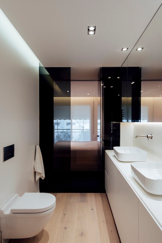 Immagine di una stanza da bagno minimalista di medie dimensioni con ante lisce, WC sospeso, pareti bianche, parquet chiaro, lavabo a bacinella, top in superficie solida e top bianco