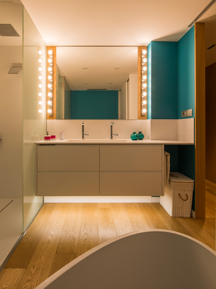 Cette image montre une salle d'eau de taille moyenne avec une baignoire indépendante, une douche à l'italienne, un mur bleu, parquet clair, un lavabo encastré et une cabine de douche à porte coulissante.
