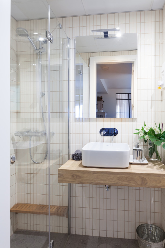 Kleines Modernes Duschbad mit offenen Schränken, hellbraunen Holzschränken, bodengleicher Dusche, Toilette mit Aufsatzspülkasten, weißen Fliesen, Keramikfliesen, weißer Wandfarbe, Keramikboden, Aufsatzwaschbecken, Waschtisch aus Holz, grauem Boden, Falttür-Duschabtrennung und brauner Waschtischplatte in Madrid