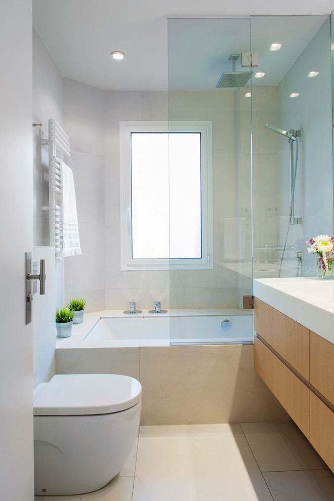 Minimalistisk inredning av ett litet en-suite badrum, med möbel-liknande, skåp i ljust trä, ett badkar i en alkov, en dusch/badkar-kombination, en toalettstol med hel cisternkåpa, klinkergolv i keramik och ett integrerad handfat