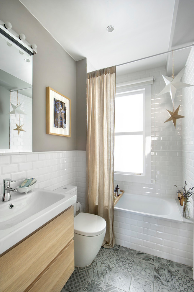Design ideas for a small eclectic ensuite bathroom in Madrid with flat-panel cabinets, light wood cabinets, an alcove bath, a shower/bath combination, a two-piece toilet, white tiles, metro tiles, grey walls, ceramic flooring, a trough sink, multi-coloured floors and a shower curtain.