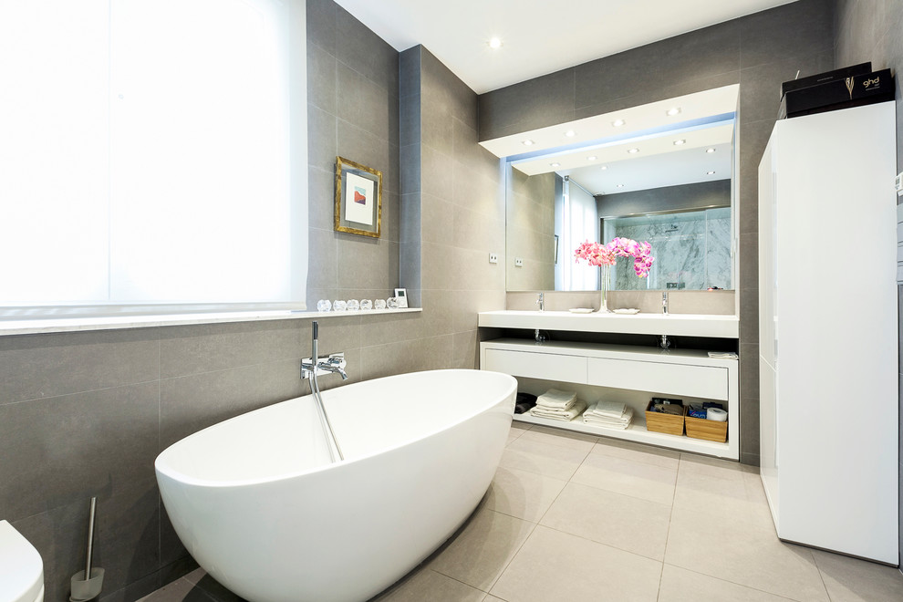 Exemple d'une salle de bain principale et grise et blanche tendance de taille moyenne avec un placard à porte plane, des portes de placard blanches, une baignoire indépendante, un combiné douche/baignoire, un mur gris, un sol en carrelage de céramique et un lavabo intégré.