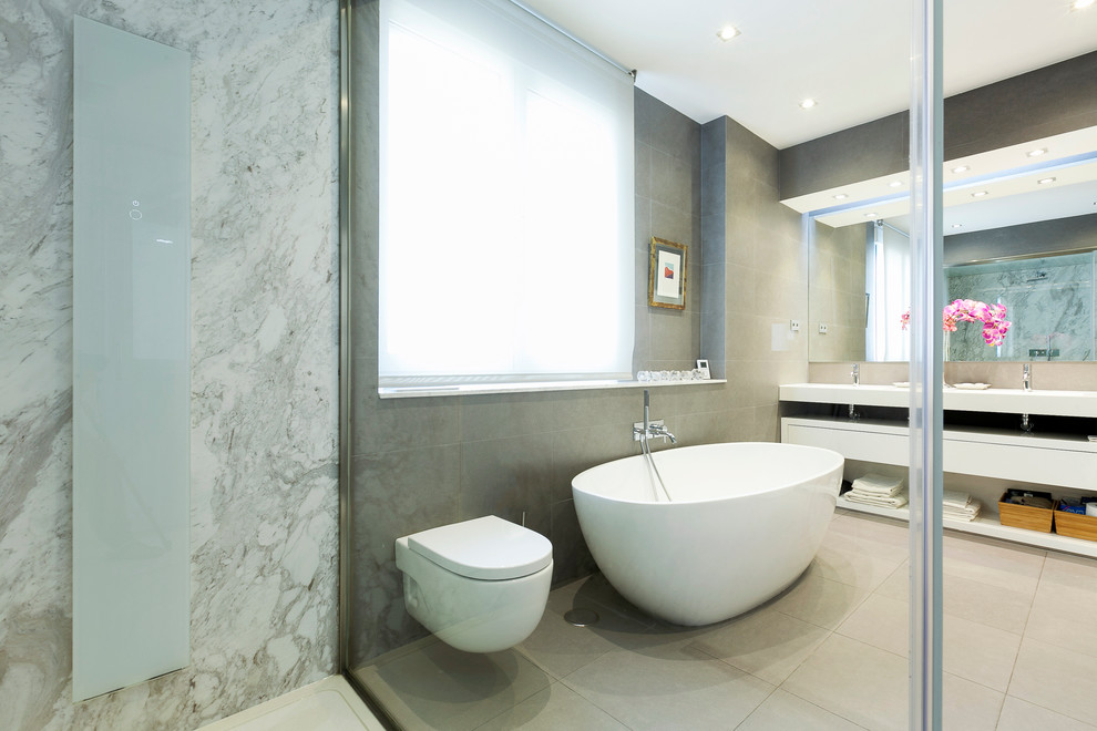 Стильный дизайн: главная ванная комната среднего размера в современном стиле с открытыми фасадами, белыми фасадами, отдельно стоящей ванной, душем над ванной, инсталляцией, серыми стенами, полом из керамической плитки и монолитной раковиной - последний тренд