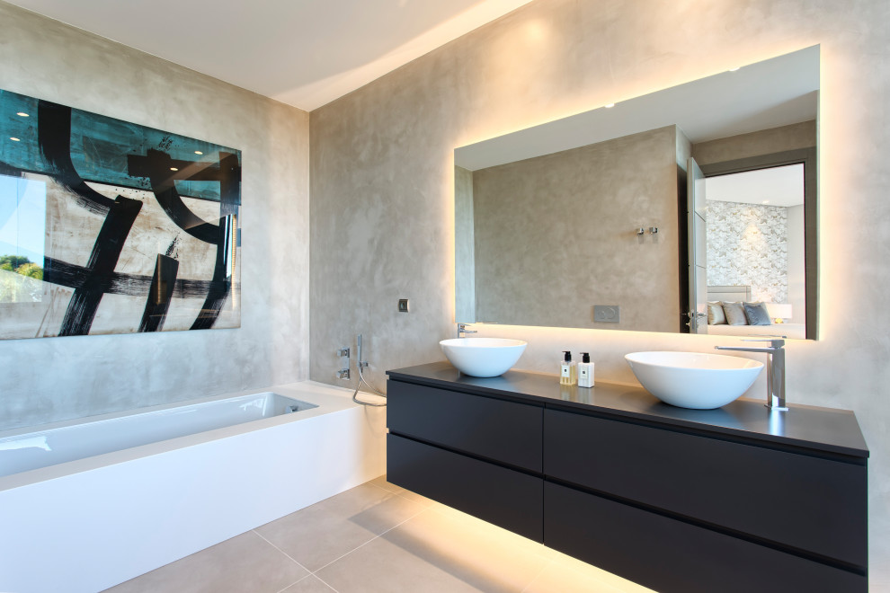 На фото: ванная комната в современном стиле с плоскими фасадами, черными фасадами, полновстраиваемой ванной, бежевыми стенами, настольной раковиной, серым полом и тумбой под две раковины с