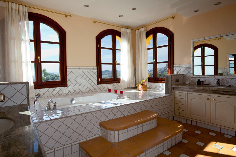Réalisation d'une grande salle de bain principale chalet avec un placard avec porte à panneau encastré, des portes de placard beiges, une baignoire posée, un combiné douche/baignoire, un mur jaune, tomettes au sol et un lavabo encastré.