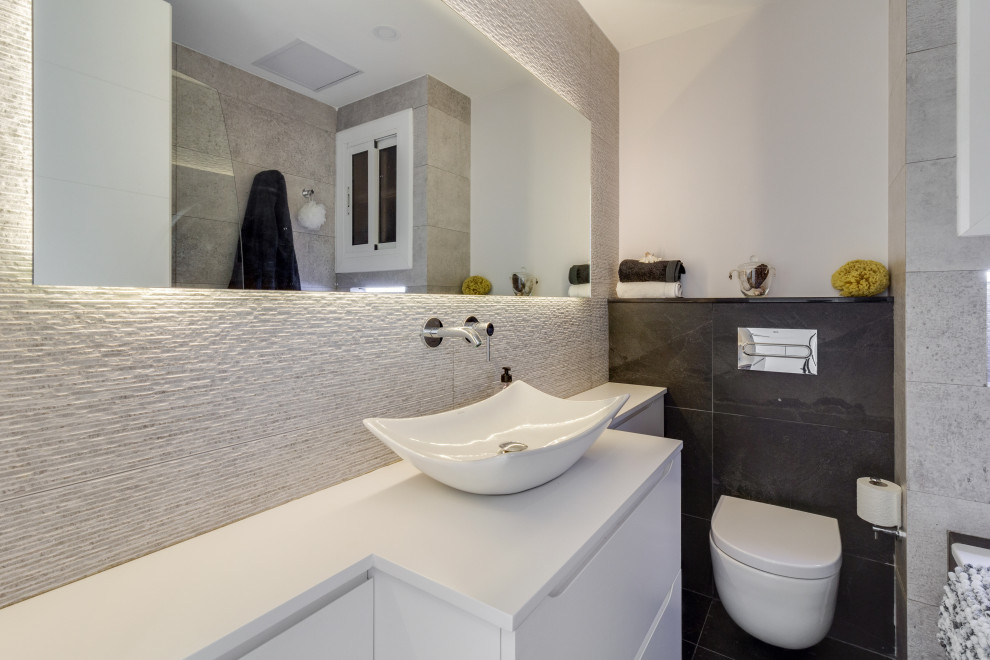 Exempel på ett litet modernt vit vitt badrum med dusch, med släta luckor, vita skåp, ett platsbyggt badkar, en dusch/badkar-kombination, en vägghängd toalettstol, grå kakel, stenkakel, vita väggar, skiffergolv, ett fristående handfat, träbänkskiva, svart golv och dusch med gångjärnsdörr