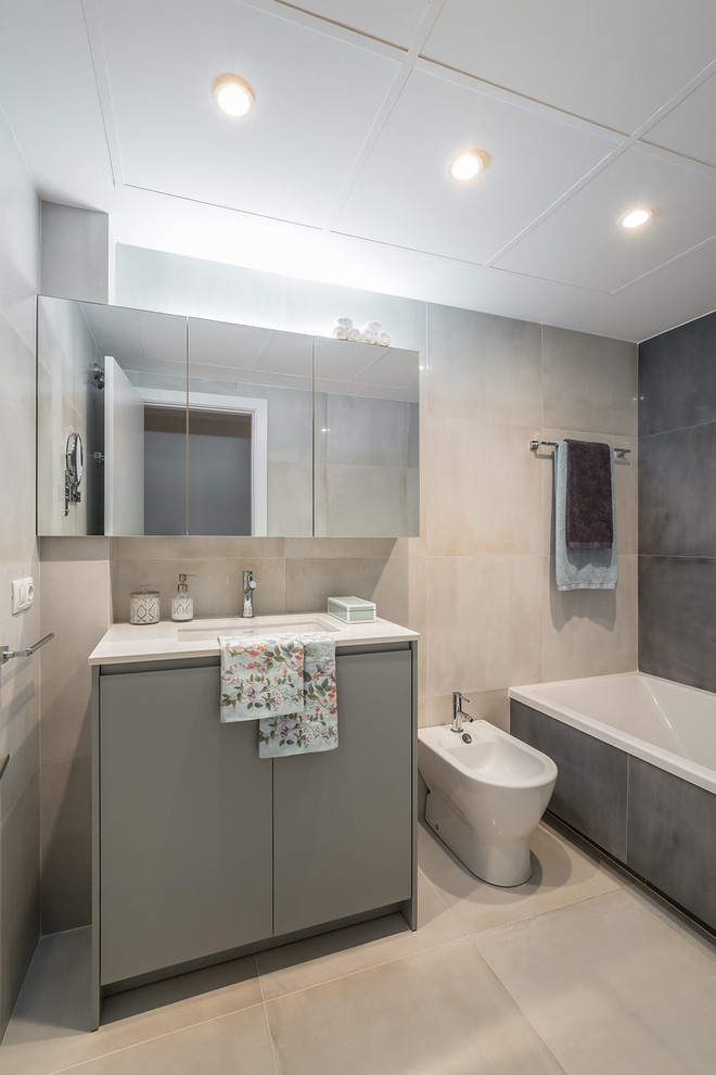 Exemple d'une salle de bain principale tendance de taille moyenne avec un placard à porte plane, des portes de placard grises, une baignoire posée, un bidet et un lavabo intégré.