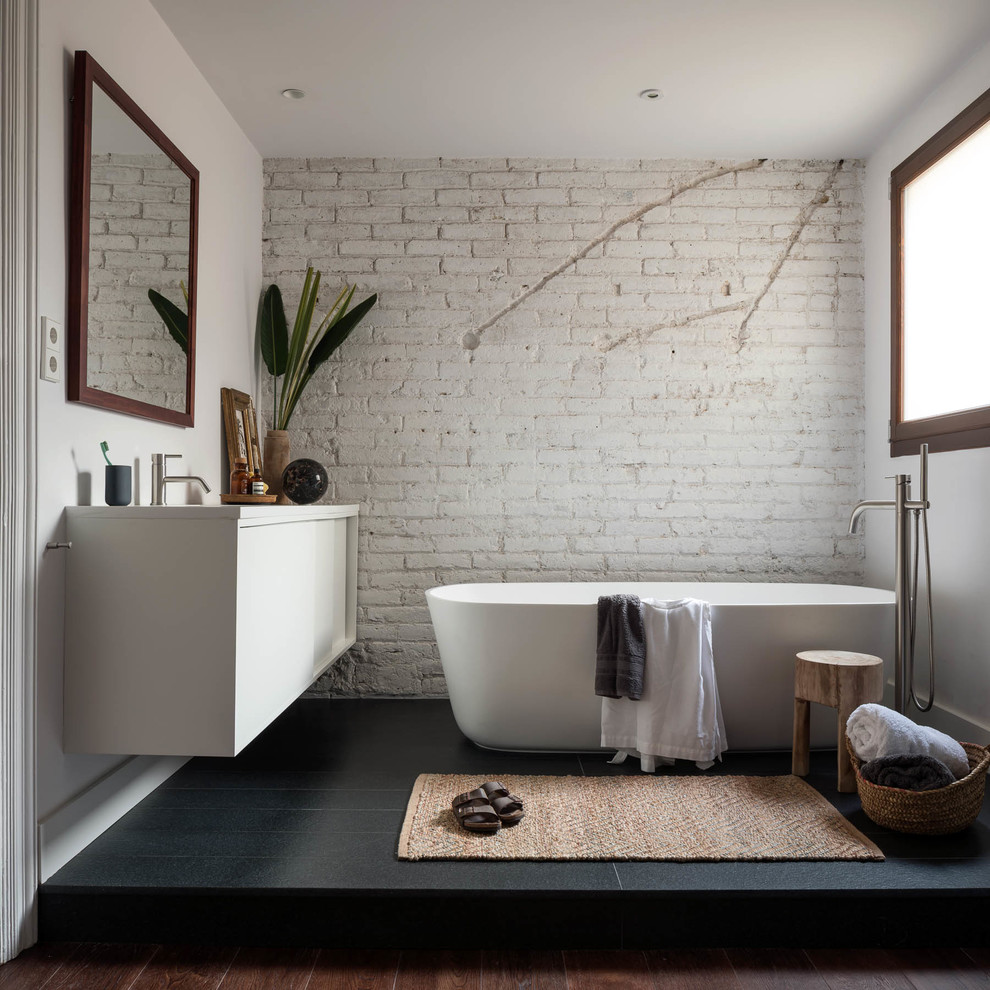 Modernes Badezimmer mit flächenbündigen Schrankfronten, weißen Schränken, freistehender Badewanne, weißer Wandfarbe, schwarzem Boden und weißer Waschtischplatte in Barcelona