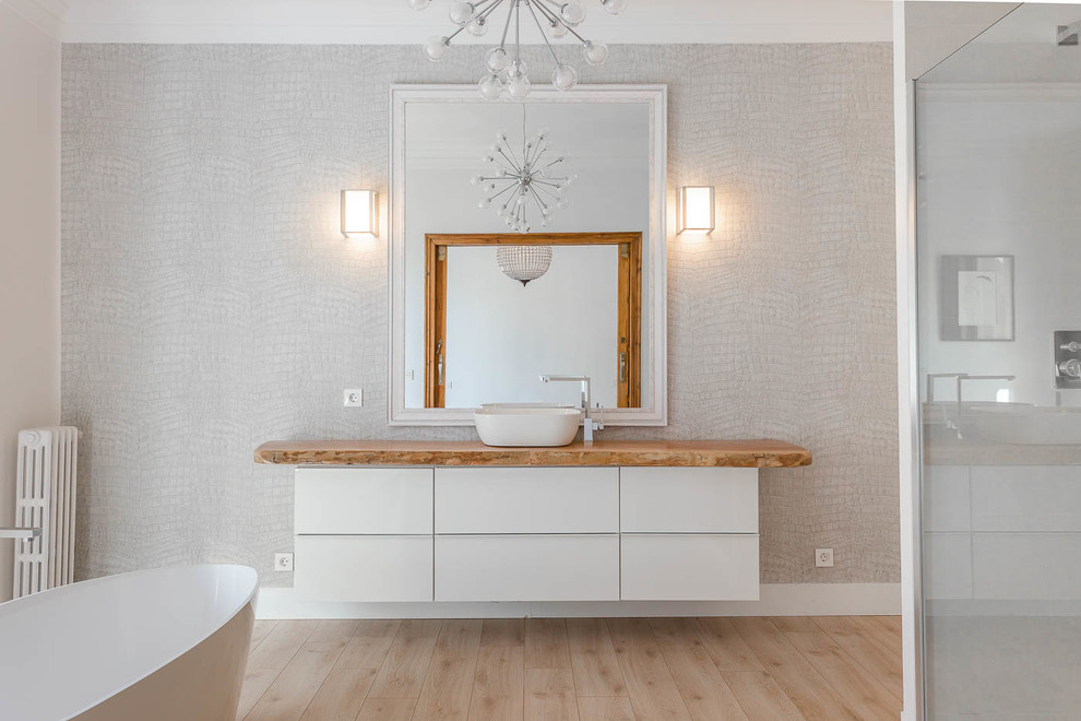 Großes Modernes Badezimmer En Suite mit beiger Wandfarbe, beigem Boden, flächenbündigen Schrankfronten, weißen Schränken, freistehender Badewanne, hellem Holzboden, Waschtischkonsole, Waschtisch aus Holz und brauner Waschtischplatte in Madrid
