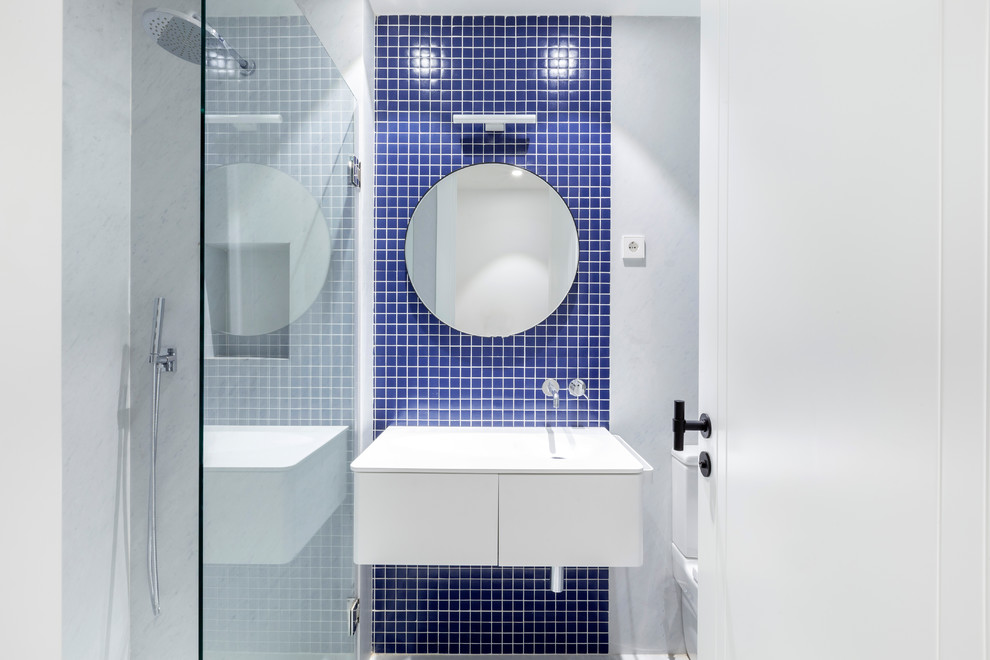 Kleines Modernes Duschbad mit flächenbündigen Schrankfronten, weißen Schränken, blauen Fliesen, Mosaikfliesen, integriertem Waschbecken und weißer Waschtischplatte in Sonstige