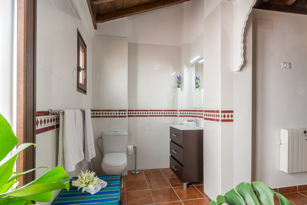 Inredning av ett klassiskt litet en-suite badrum, med möbel-liknande, bruna skåp, en kantlös dusch, en toalettstol med hel cisternkåpa, vit kakel, keramikplattor, vita väggar, klinkergolv i terrakotta, ett fristående handfat, brunt golv och med dusch som är öppen