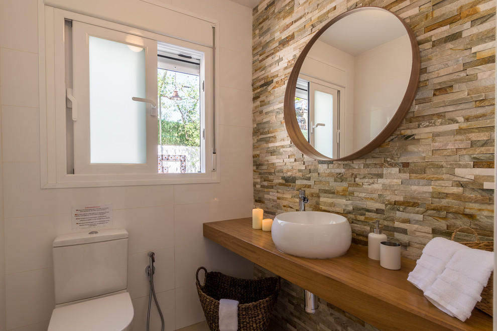 Photo of a small mediterranean bathroom in Other with open cabinets, brown cabinets, a one-piece toilet, white tiles, ceramic tiles, white walls, ceramic flooring, a vessel sink, wooden worktops and beige floors.