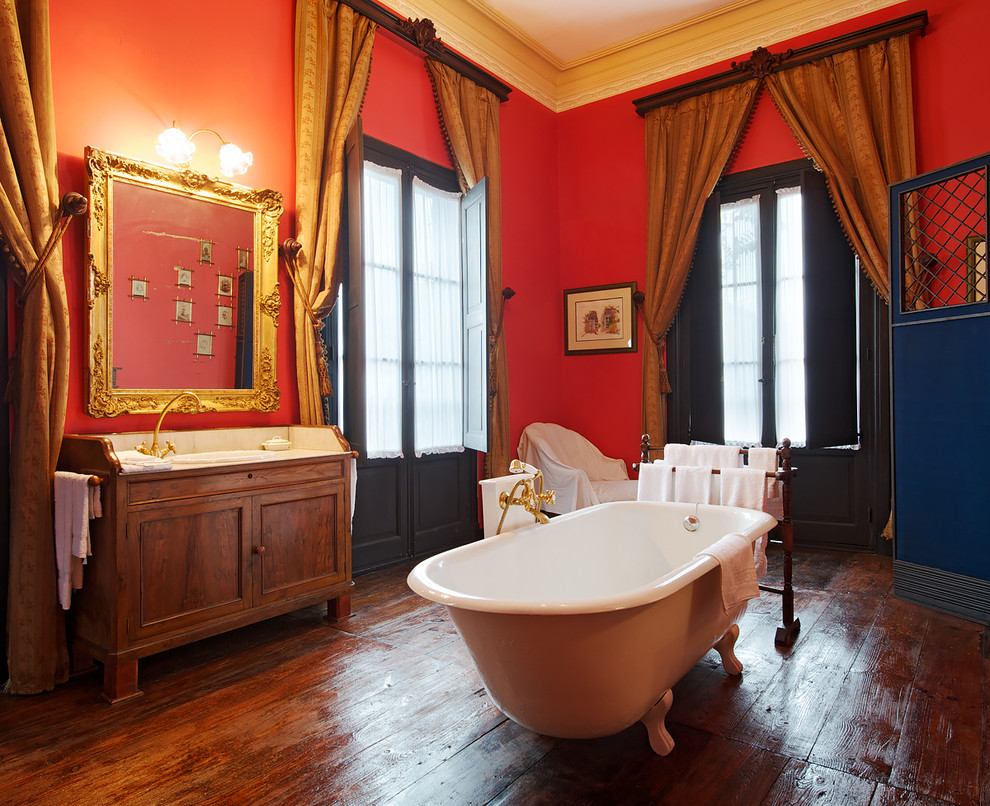 他の地域にある高級な中くらいなトラディショナルスタイルのおしゃれな浴室 (レイズドパネル扉のキャビネット、濃色木目調キャビネット、猫足バスタブ、シャワー付き浴槽	、赤い壁、濃色無垢フローリング、オーバーカウンターシンク) の写真