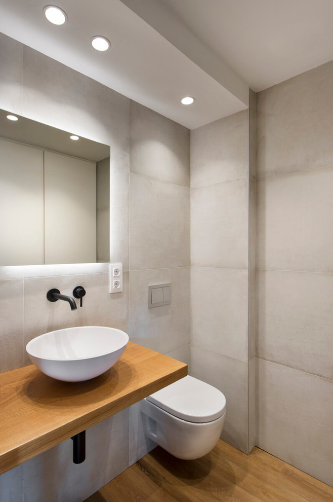 Aménagement d'une salle de bain moderne avec un carrelage beige, un mur beige, un sol en bois brun, une vasque, un plan de toilette en bois, un sol marron et un plan de toilette marron.