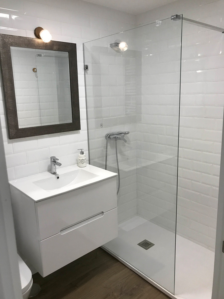Foto på ett litet funkis vit badrum med dusch, med en dusch i en alkov, en toalettstol med separat cisternkåpa, vit kakel, keramikplattor, vita väggar, laminatgolv, ett väggmonterat handfat, bänkskiva i kvarts, brunt golv och dusch med skjutdörr