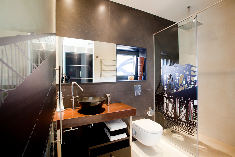 Bild på ett mellanstort funkis badrum med dusch, med öppna hyllor, skåp i mörkt trä, en kantlös dusch, en vägghängd toalettstol, cementkakel, grå väggar, ett fristående handfat och träbänkskiva