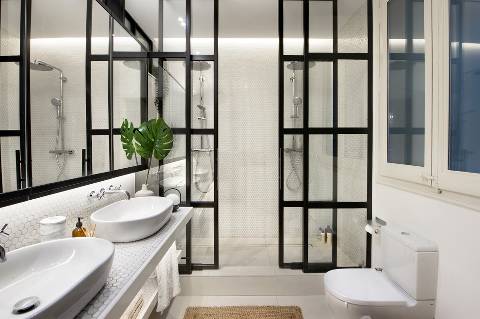 Bild på ett funkis vit vitt badrum med dusch, med öppna hyllor, vita skåp, en dubbeldusch, en toalettstol med separat cisternkåpa, vita väggar, ett fristående handfat, kaklad bänkskiva, vitt golv och dusch med skjutdörr