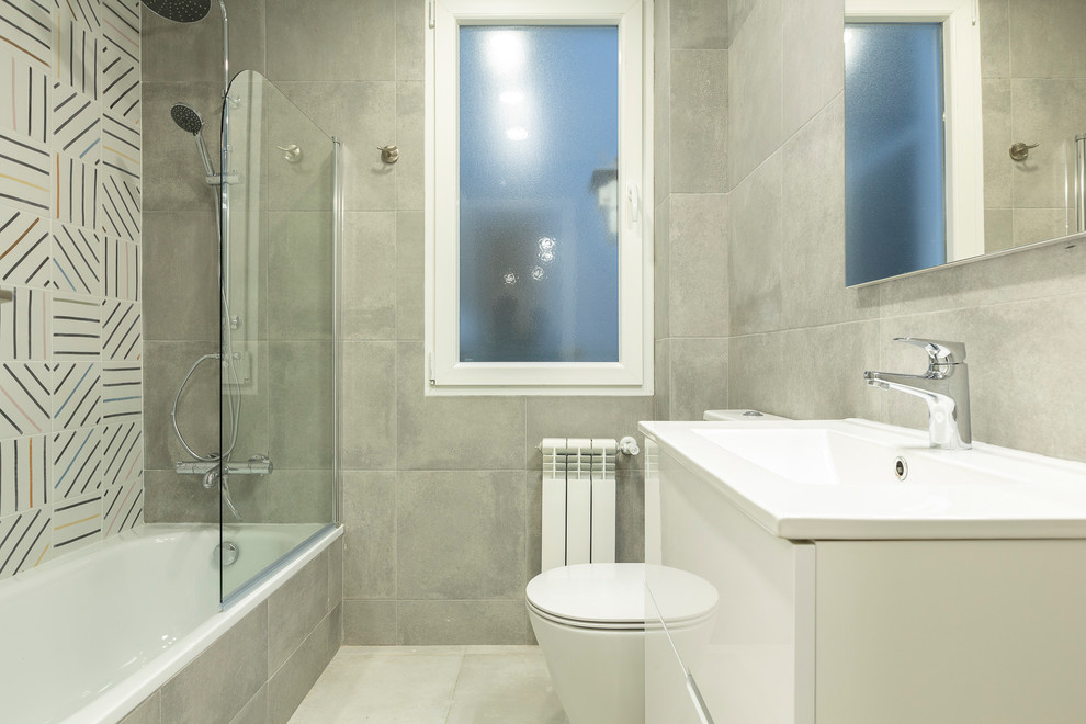 Идея дизайна: ванная комната среднего размера в стиле модернизм с фасадами островного типа, белыми фасадами, накладной ванной, душем над ванной, унитазом-моноблоком, белой плиткой, керамогранитной плиткой, серыми стенами, полом из керамогранита, душевой кабиной, раковиной с несколькими смесителями, столешницей из искусственного камня, серым полом, душем с распашными дверями и белой столешницей