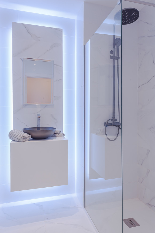 Bild på ett funkis vit vitt badrum, med släta luckor, vita skåp, en kantlös dusch, vita väggar, ett fristående handfat, vitt golv och med dusch som är öppen