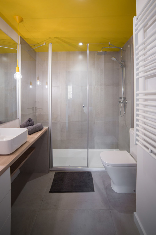 Design ideas for a medium sized contemporary grey and yellow shower room bathroom in Barcelona with grey tiles, cement tiles, cement flooring, a vessel sink, wooden worktops, grey floors, a hinged door, flat-panel cabinets, white cabinets, an alcove shower, a two-piece toilet and white walls.