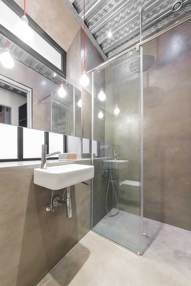 Modelo de cuarto de baño urbano de tamaño medio con ducha a ras de suelo, paredes grises, suelo de cemento, aseo y ducha, lavabo suspendido, ducha abierta y microcemento