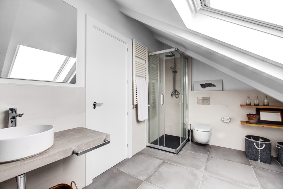 Diseño de cuarto de baño actual con baldosas y/o azulejos grises, aseo y ducha, lavabo sobreencimera, ducha con puerta corredera, ducha esquinera, sanitario de pared, paredes beige, encimera de cemento, suelo gris y encimeras grises