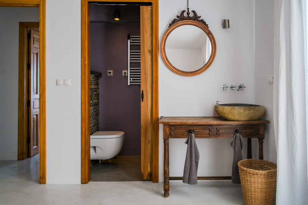 Réalisation d'une petite salle de bain méditerranéenne en bois brun avec une vasque, WC suspendus, un mur violet, sol en béton ciré, un plan de toilette en bois et un placard avec porte à panneau encastré.