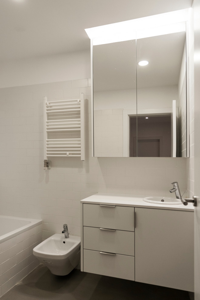 Ispirazione per una piccola stanza da bagno padronale industriale con ante lisce, ante bianche, vasca ad alcova, vasca/doccia, bidè e lavabo sottopiano