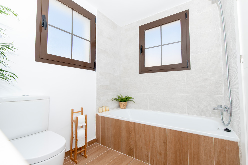 This is an example of a small mediterranean bathroom in Malaga with flat-panel cabinets, white cabinets, an alcove bath, a wall mounted toilet, white tiles, ceramic tiles, white walls, porcelain flooring, a submerged sink, laminate worktops, brown floors and white worktops.