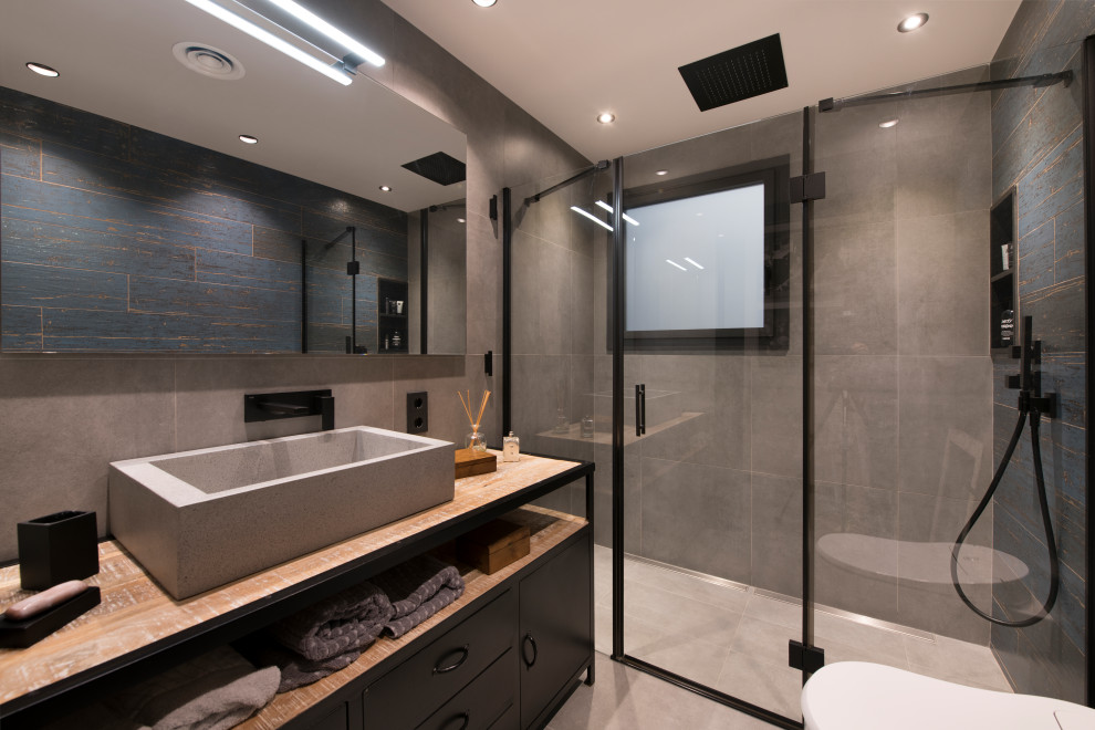 Idéer för stora industriella brunt badrum med dusch, med öppna hyllor, grå skåp, en dusch i en alkov, en vägghängd toalettstol, grå kakel, porslinskakel, blå väggar, klinkergolv i porslin, ett fristående handfat, träbänkskiva, grått golv och dusch med gångjärnsdörr