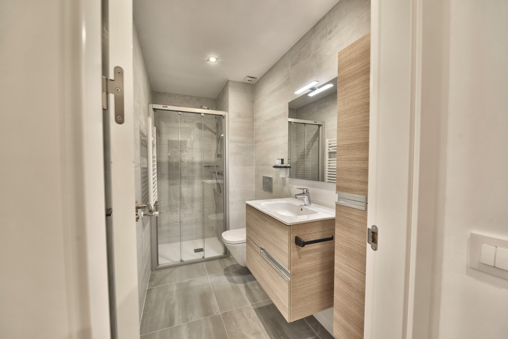 Bild på ett mellanstort nordiskt badrum med dusch, med släta luckor, vita skåp, en kantlös dusch, grå kakel, keramikplattor, vita väggar, laminatgolv, grått golv och dusch med skjutdörr