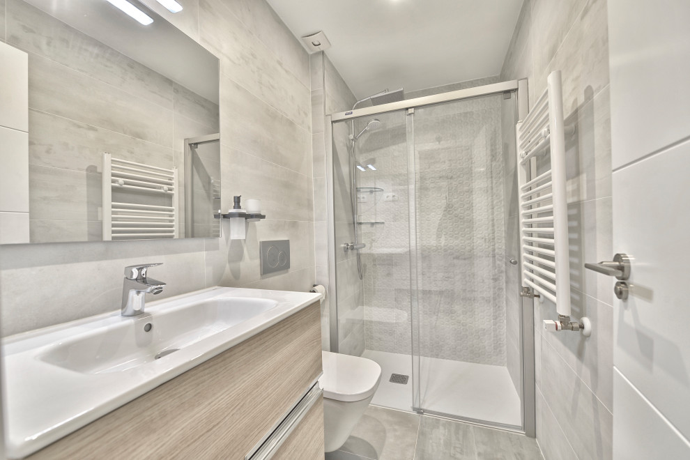 Medium sized scandinavian shower room bathroom in Madrid with flat-panel cabinets, white cabinets, a built-in shower, grey tiles, ceramic tiles, white walls, laminate floors, grey floors, a sliding door, an enclosed toilet and a single sink.